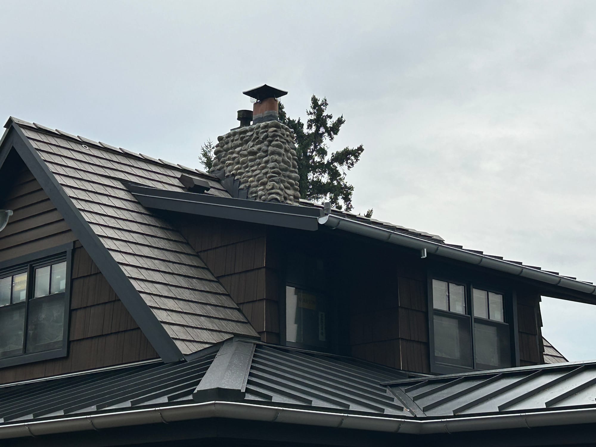 Shake-look upper roof, stone chimney and dark metal lower roof sections