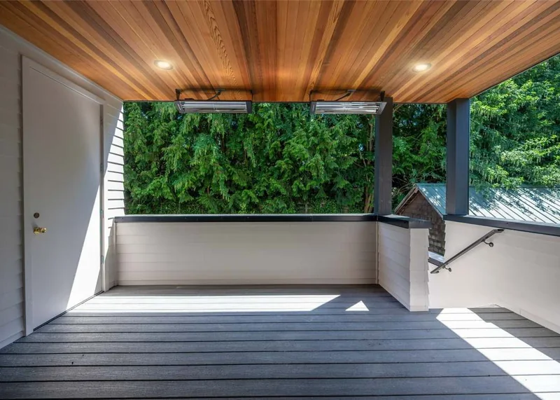 Covered deck at 5620 6th Avenue NW with wood-plank ceiling, overhead heaters, composite floor and evergreen backdrop